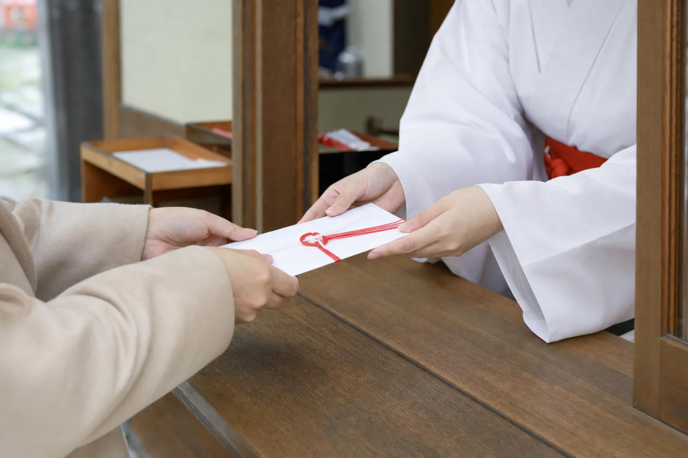 神社の受付で初穂料ののし袋を両手で渡す様子